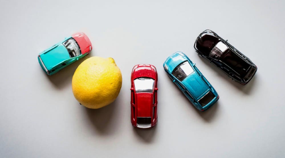 Lemon law attorney with four toy cars and a lemon on a white background.