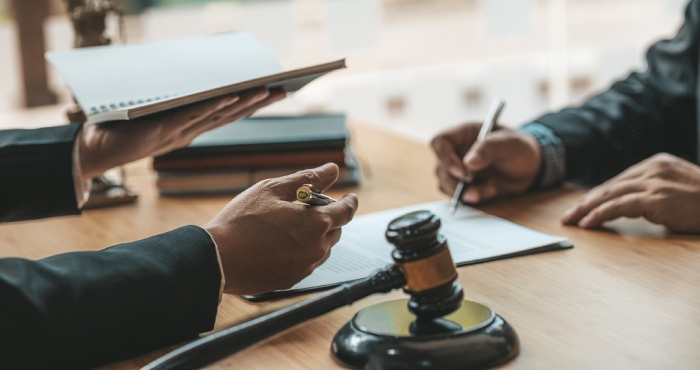A lawyer's gavel rests on a desk alongside a book and a pen.