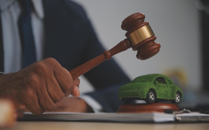A person in a suit is signing a document at a desk adorned with a gavel and a red notebook, pondering, "What is the California Lemon Law?.