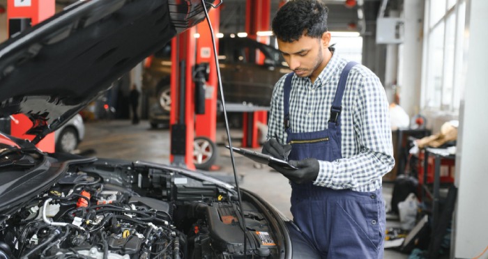 A man examines the engine of a white car with the hood open, parked on the roadside, perhaps wishing he had consulted a California lemon law attorney before hitting the road.