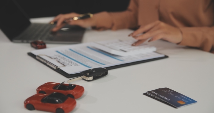 A person types on a laptop next to a clipboard, calculator, credit card, and two toy cars on a desk, preparing documents for lemon law attorneys known for their courtroom success.