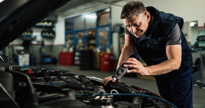 A mechanic inspects a car engine with a flashlight in a garage, ensuring all vehicle modifications comply with the California Lemon Law.