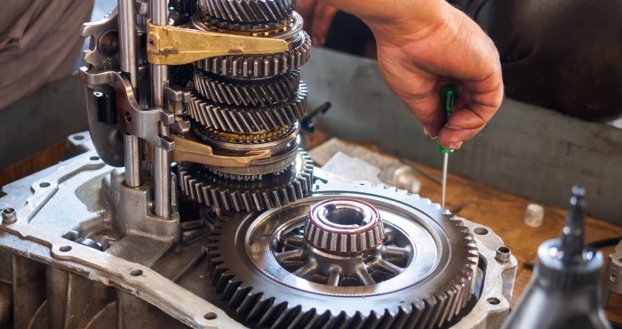 In a scene reminiscent of the meticulous precision found in courtroom success, a person is skillfully adjusting a car transmission gearbox with a small screwdriver. Exposed gears and mechanical components scatter across the workbench like evidence awaiting examination.