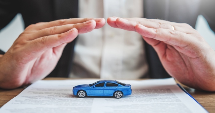 Hands hover protectively over a blue toy car placed on a document, symbolizing the security offered by California Lemon Law.