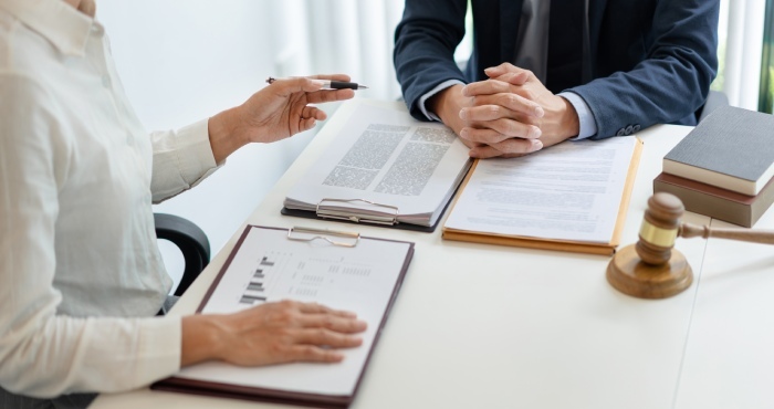 Two people at a desk, surrounded by documents and a gavel, exude confidence. One holds a pen poised for action while the other clasps their hands thoughtfully—picture-perfect Lemon Law attorneys ready to achieve courtroom success.